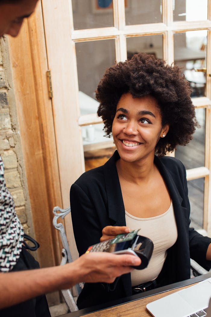 awards-img Woman with afro hairstyle makes a payment at a cafe using a wireless card terminal, smiling.